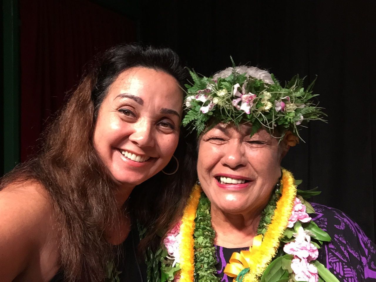 Two women are posing for a picture together and one of them is wearing a lei.