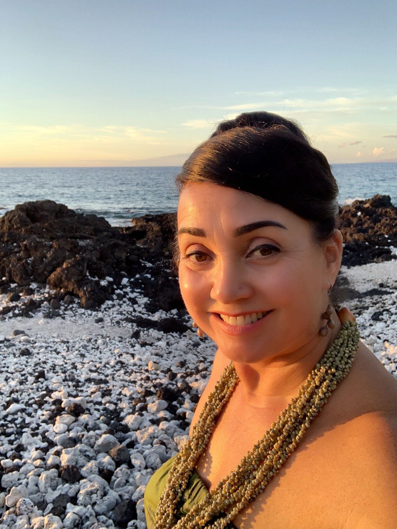 A woman is standing on a rocky beach near the ocean.