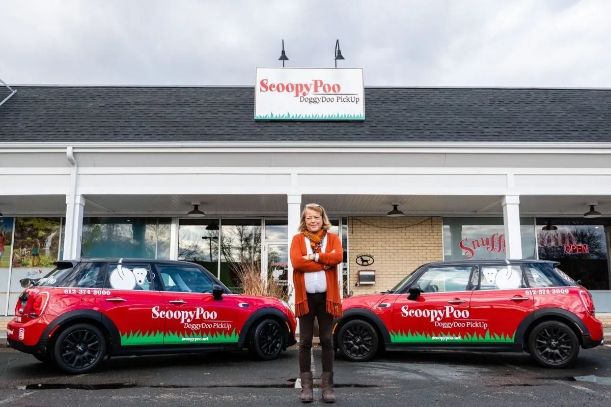 Woman standing between two red ScoopyPoo cars in front of a storefront.