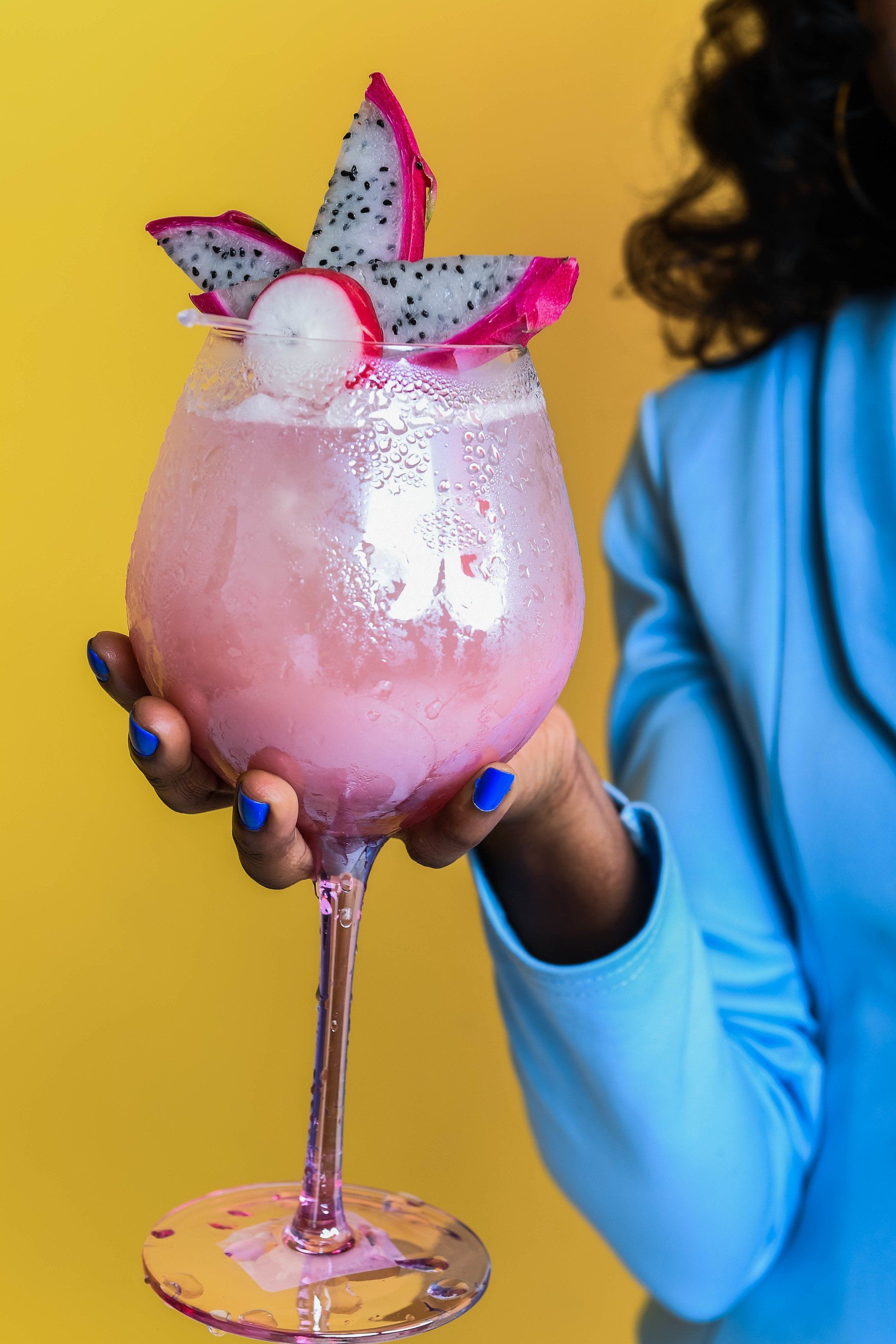 A woman is holding a glass of pink liquid with a dragon fruit on top.