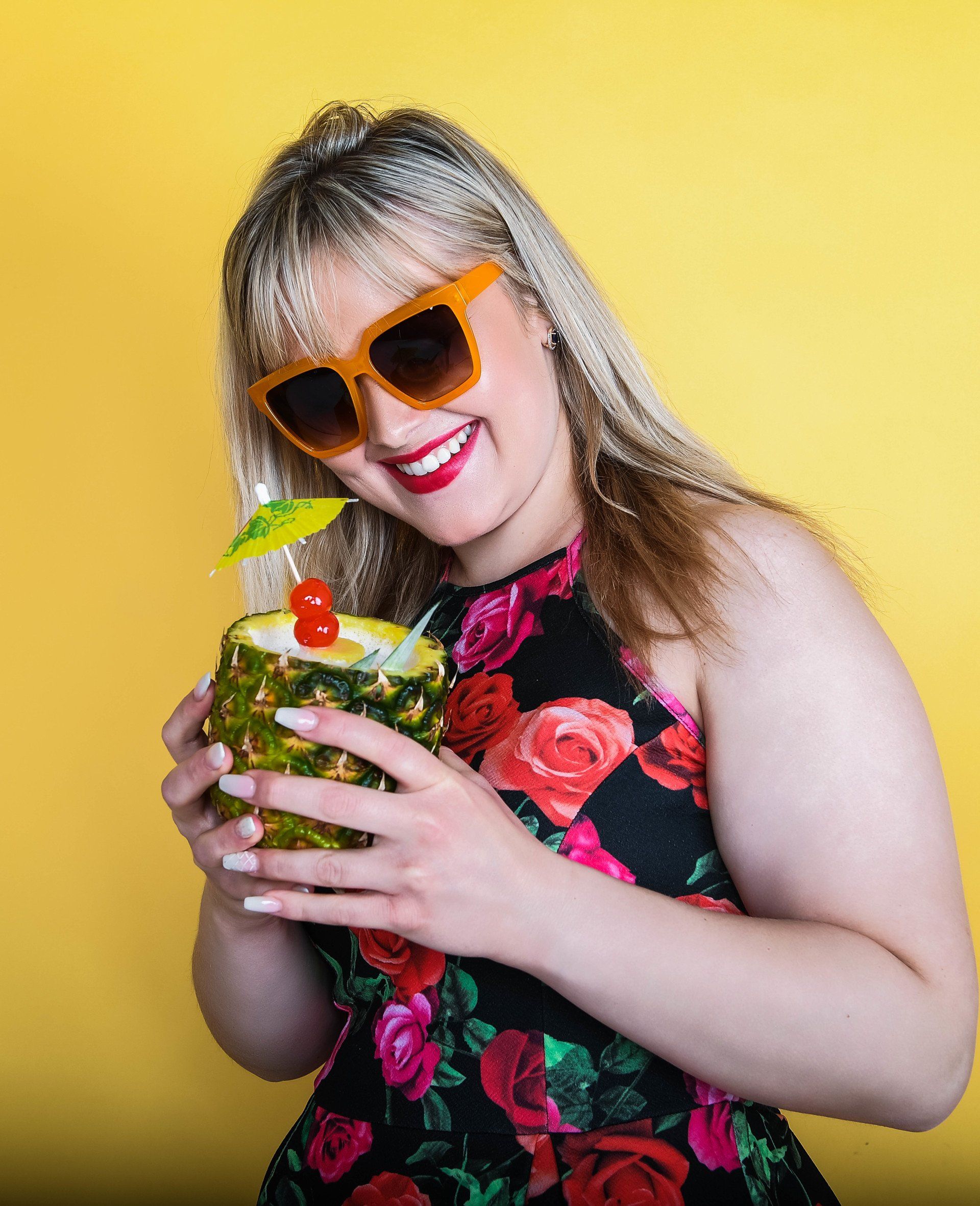 A woman wearing sunglasses is holding a pineapple with a drink in it.