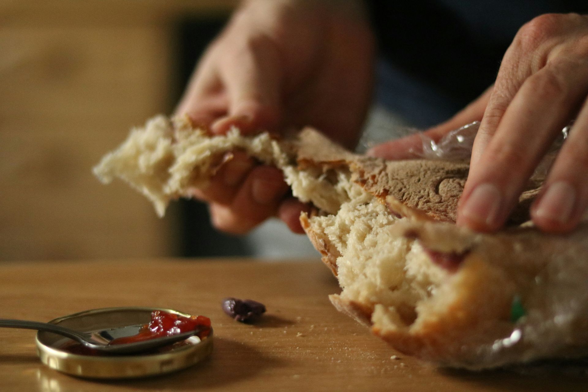 Hände zerreißen ein Brot, auf dem ein kleiner Metalldeckel einen Löffel rote Soße auf einer Holzoberfläche hält.
