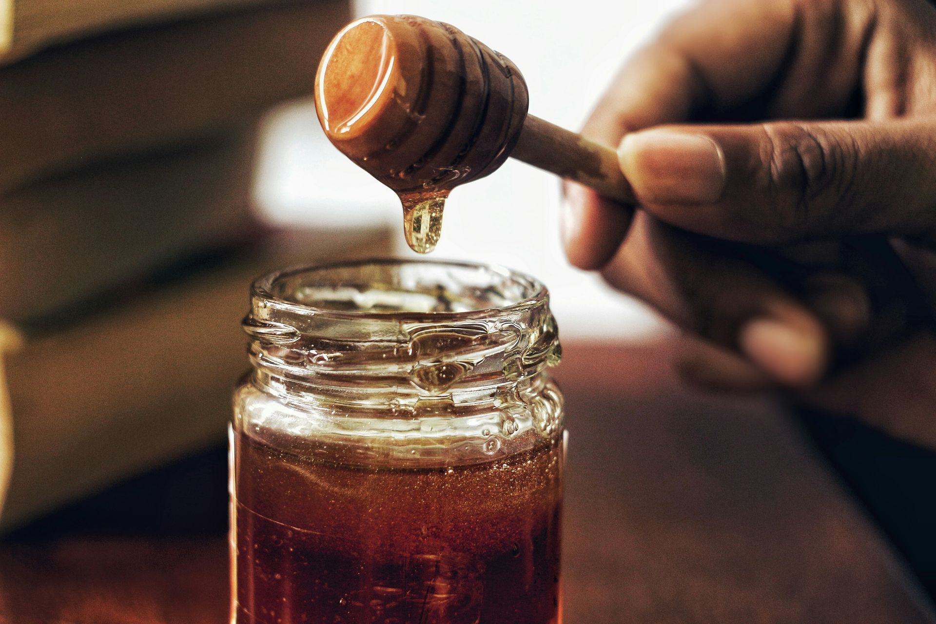 Ein hölzerner Honiglöffel wurde über ein offenes Glas mit goldenem Honig gehalten, aus dessen Rillen ein einzelner Tropfen tropfte.
