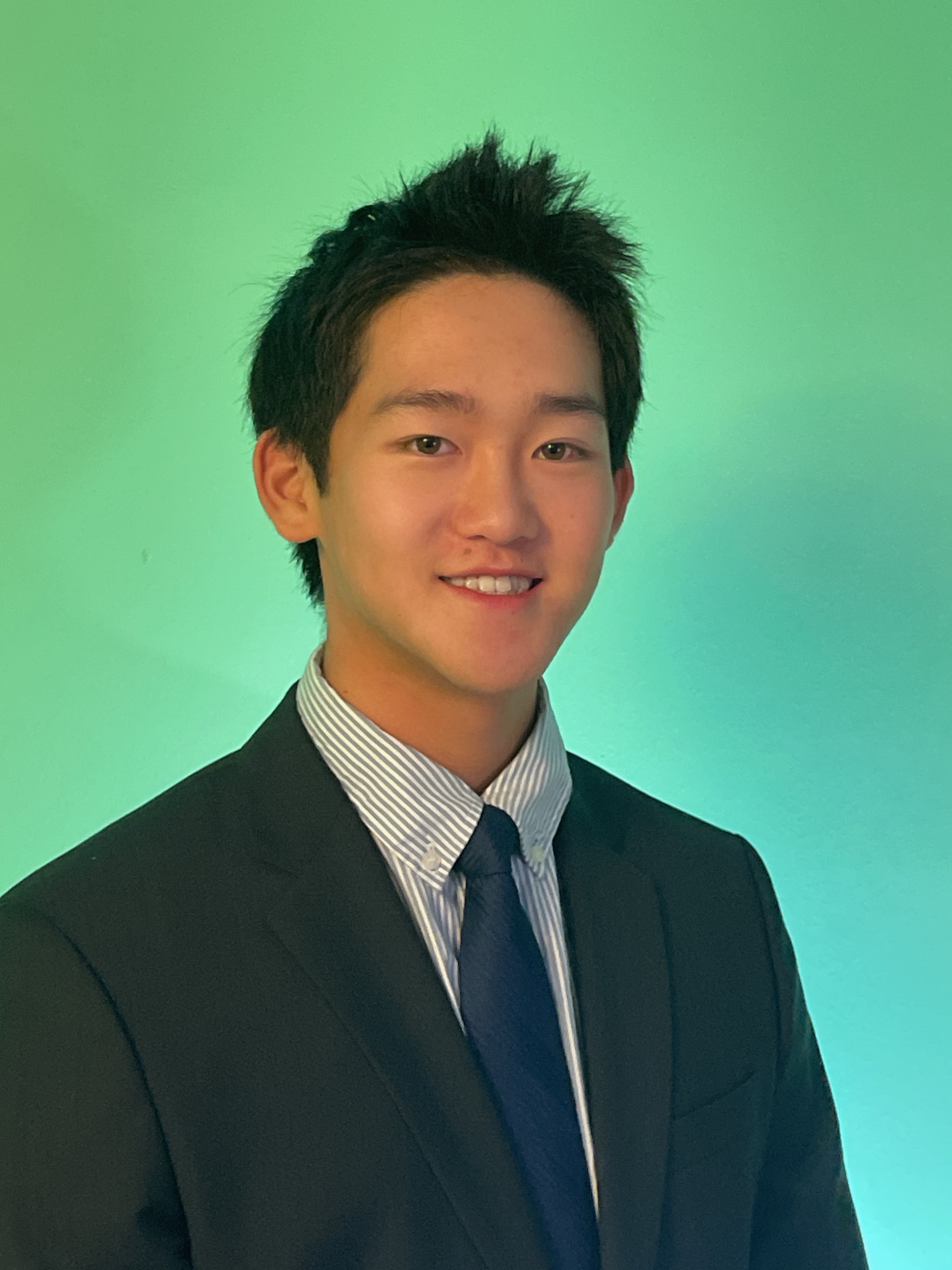 Man with glasses wearing a suit jacket and white shirt against a gradient gray backdrop.