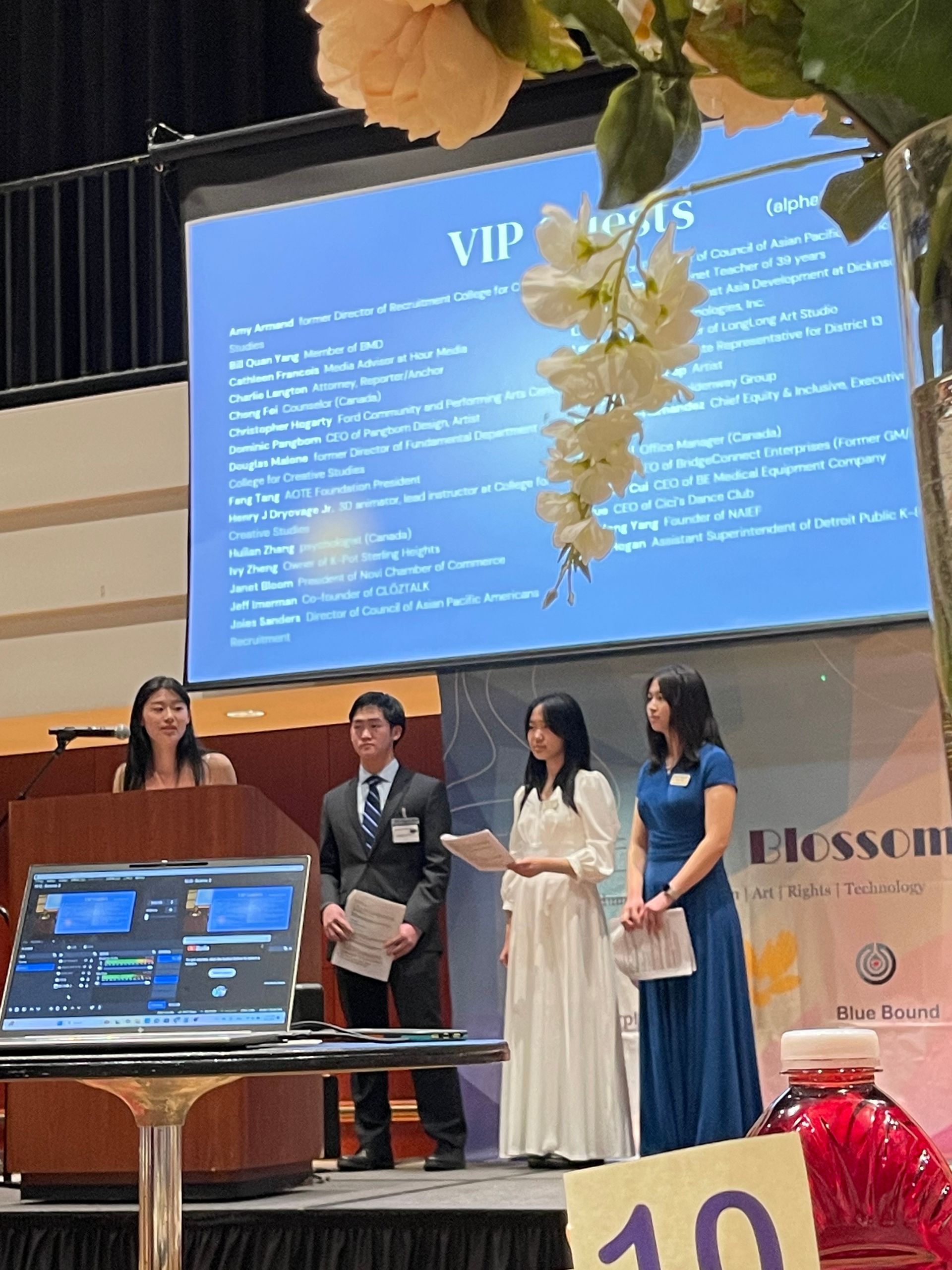 Four people present on a stage with a screen behind them. The screen lists VIP guests.