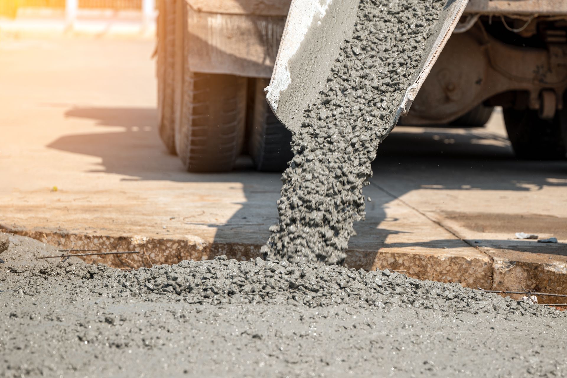 Close-up of wet concrete being poured into a construction site, under the sun.