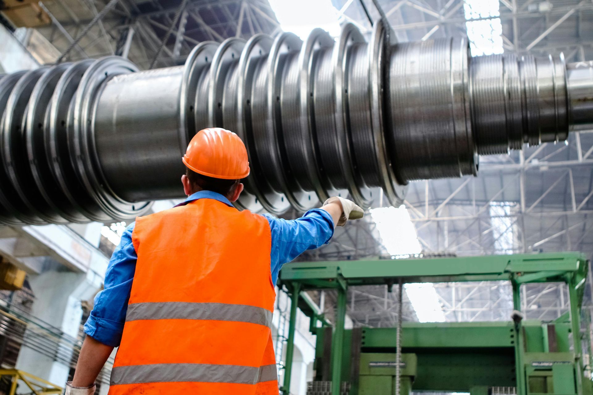 Worker in orange vest inspecting a large industrial turbine in a factory.