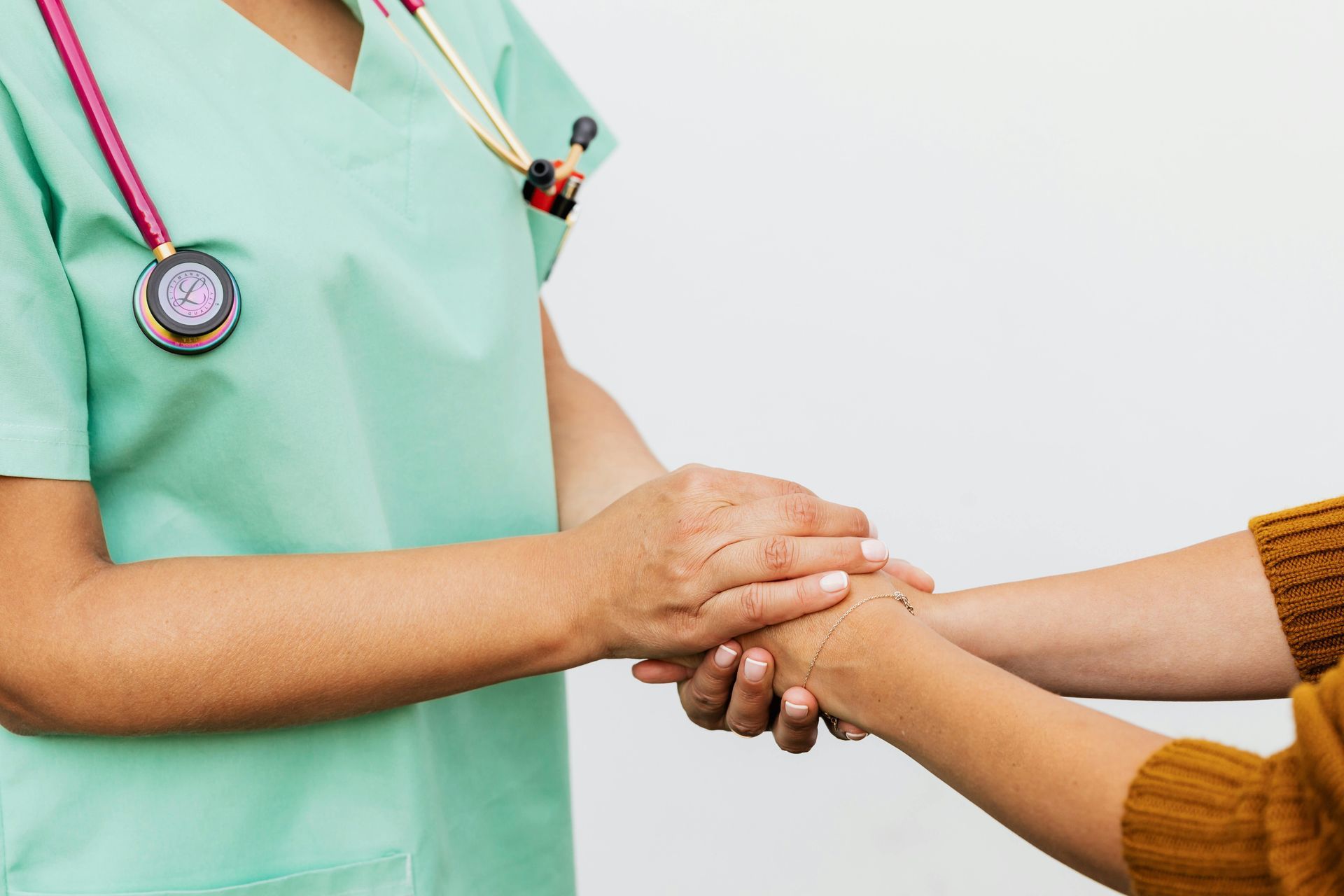 Nurse in green scrubs holding a patient's hand for comfort.
