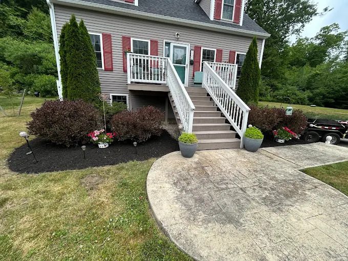 Front yard of a red house with white stairs, porch, and curved concrete driveway