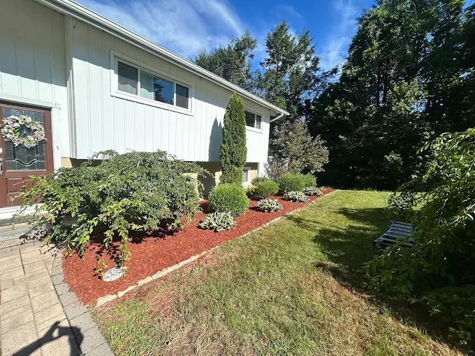 Suburban house exterior with landscaped flower beds, shrubs, and a grassy lawn in bright sunlight