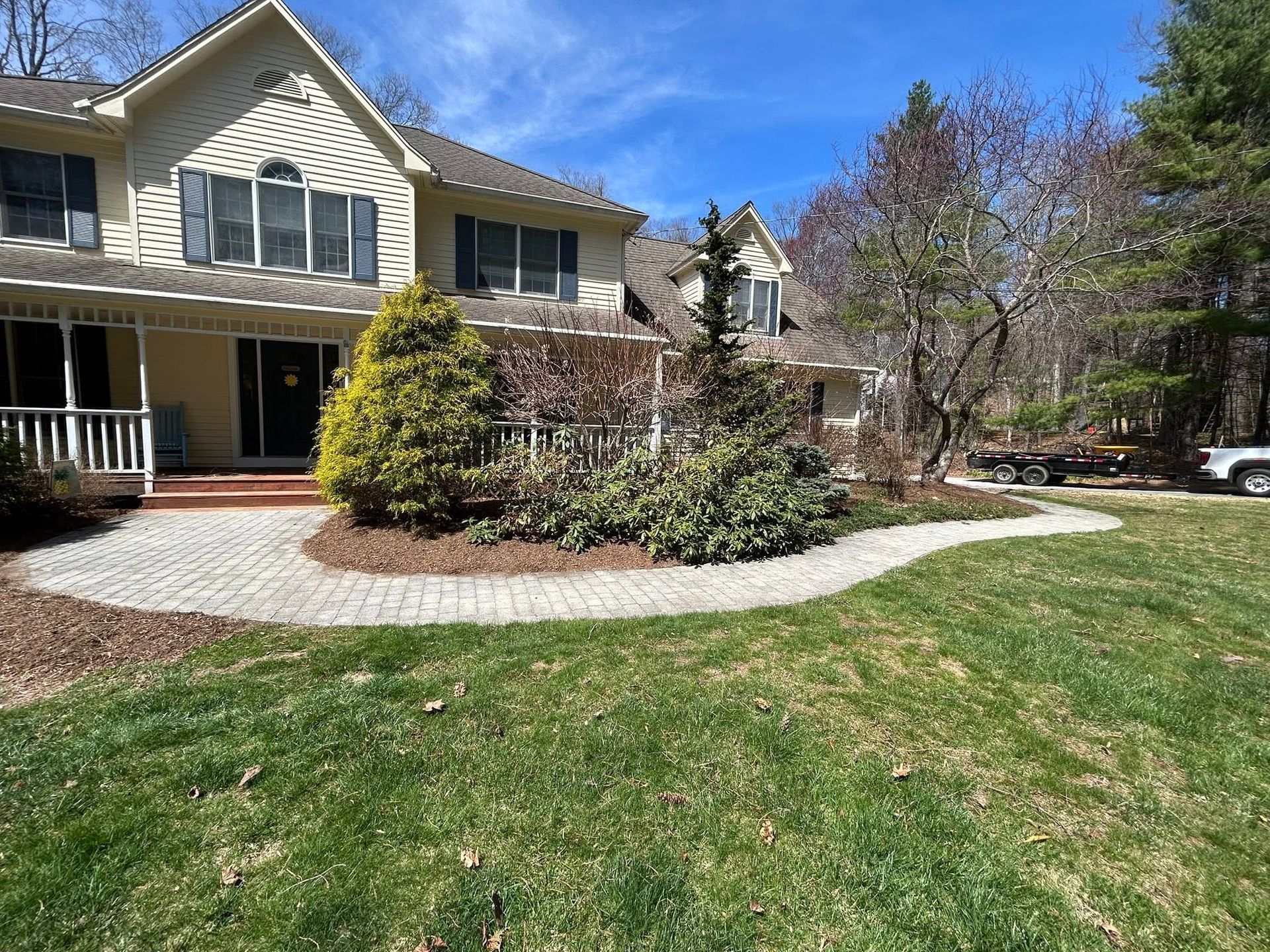 Suburban house with front porch, shrubs, and a curved walkway beside a green lawn under a blue sky