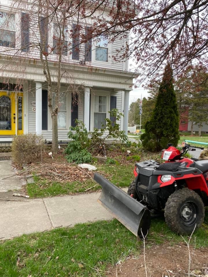 Red ATV with snowplow parked on a sidewalk beside a house and yard