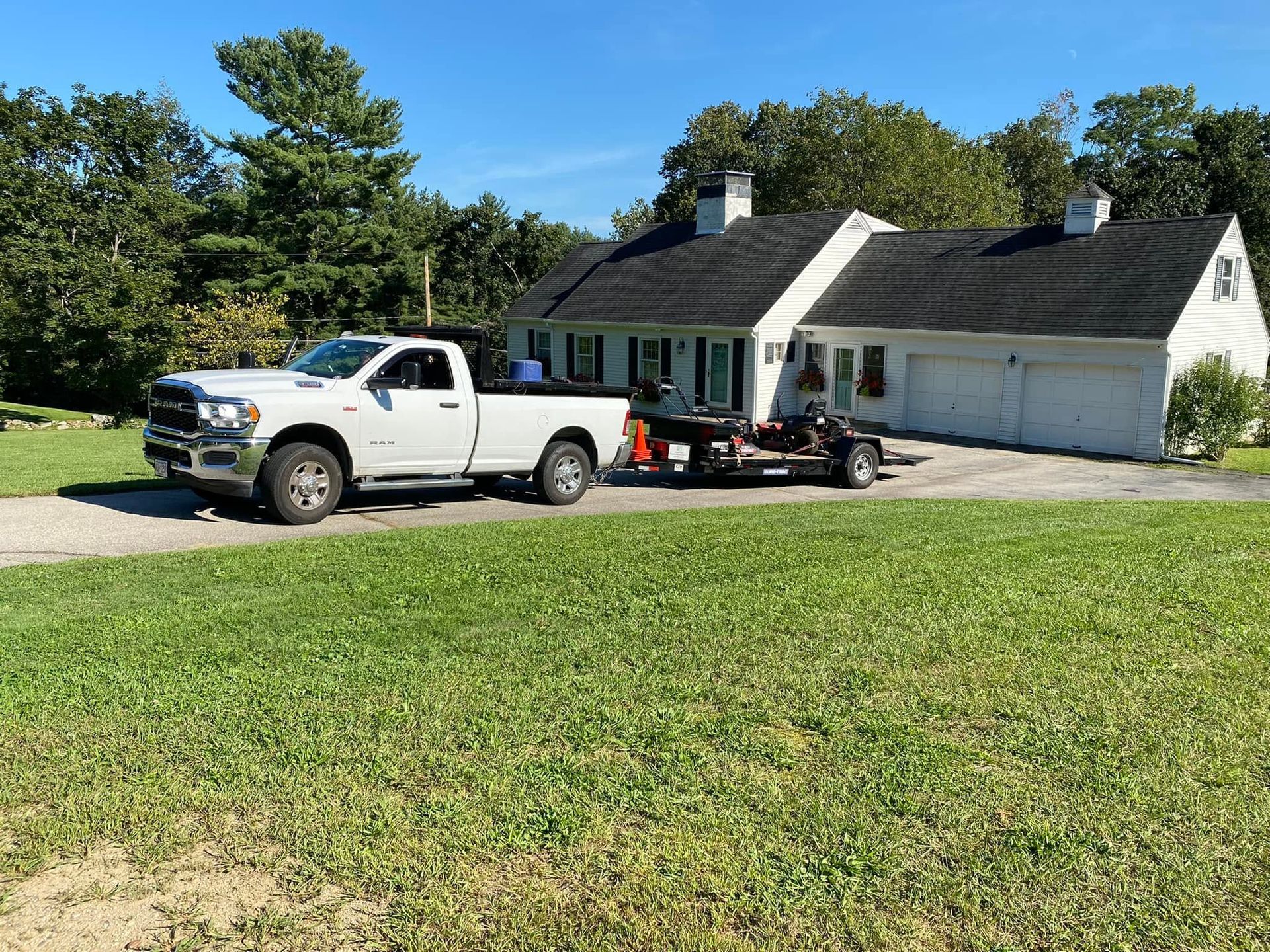 White pickup truck with trailer parked beside a white house on a sunny rural lawn
