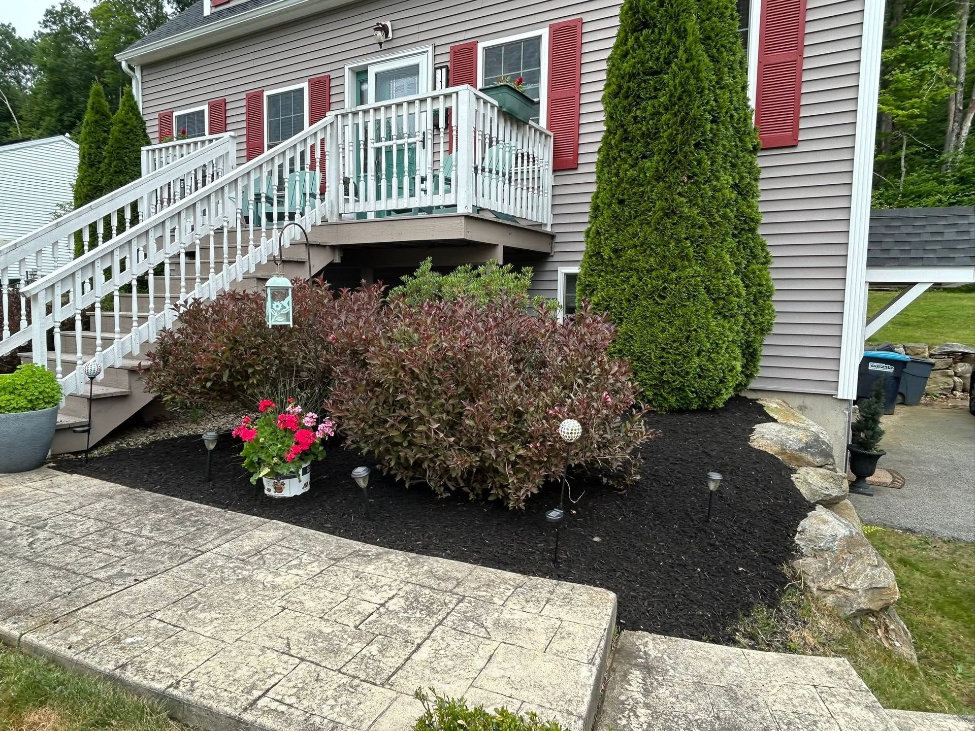 House with white staircase, red shutters, and flower bed in front of a brick walkway