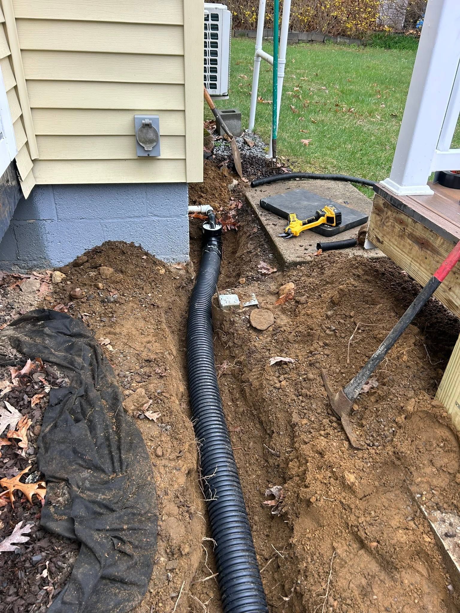 Trench with black conduit laid beside a house during utility or drainage work