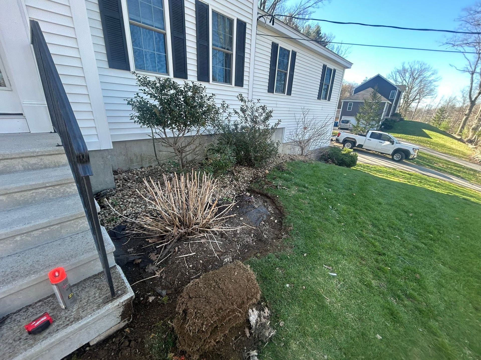 Front yard beside a white house with shrubs, mulch, and a red level tool on steps.