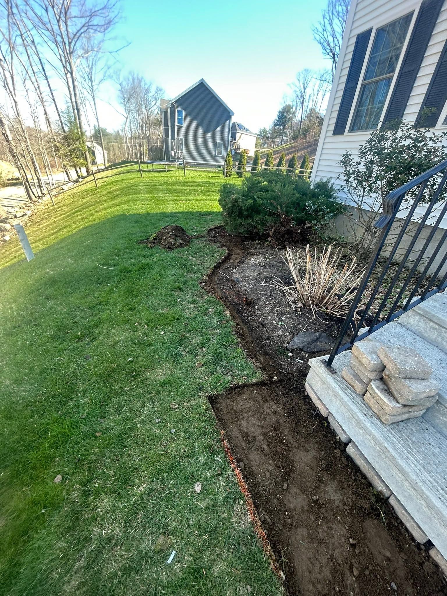 Backyard lawn with a narrow mulch bed beside a house and shrubs, viewed on a sunny day