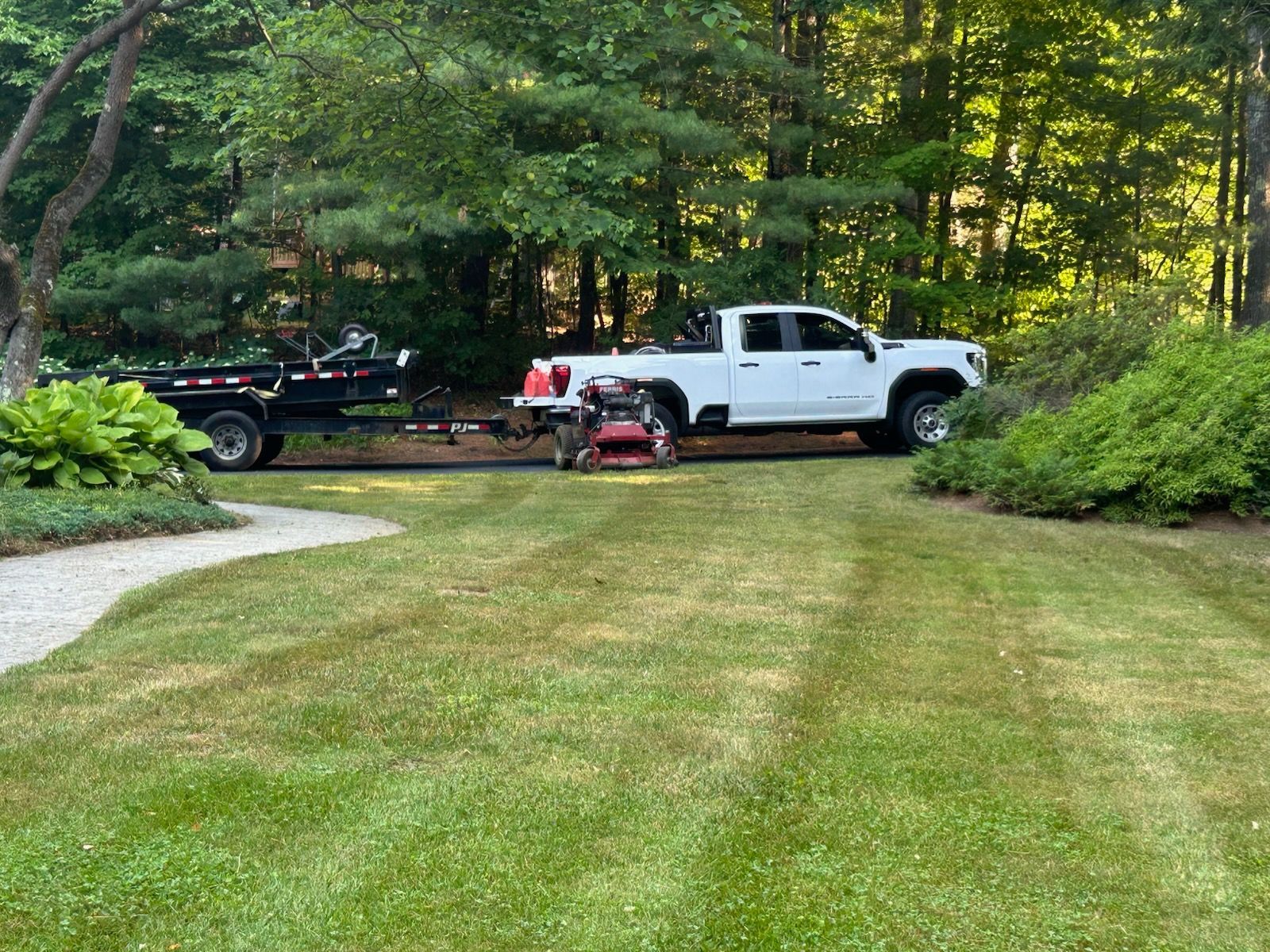 White pickup and black truck parked on a grassy driveway by a wooded yard
