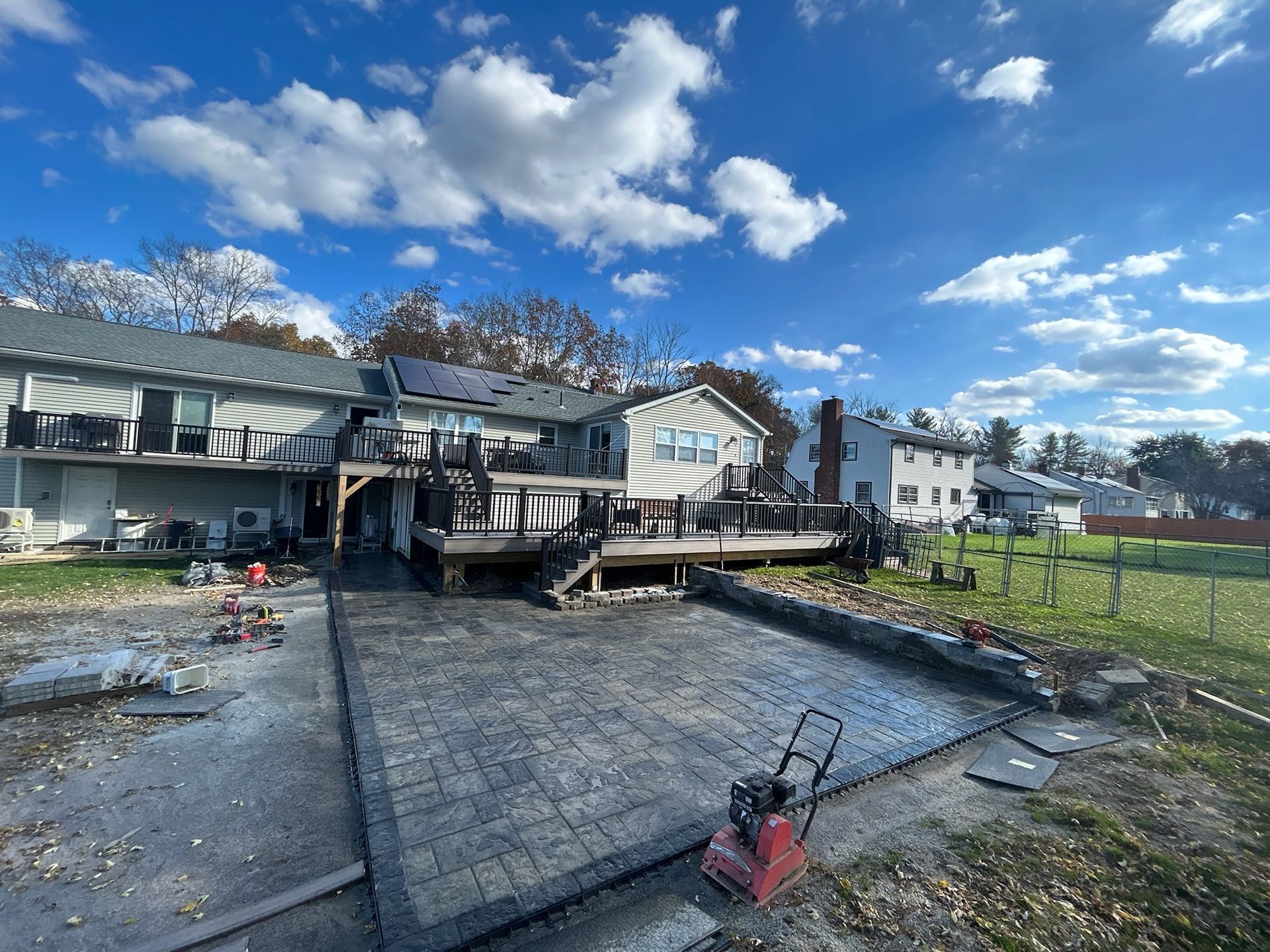 Damaged backyard deck and patio after storm, with debris, tilted railing, and cloudy blue sky.