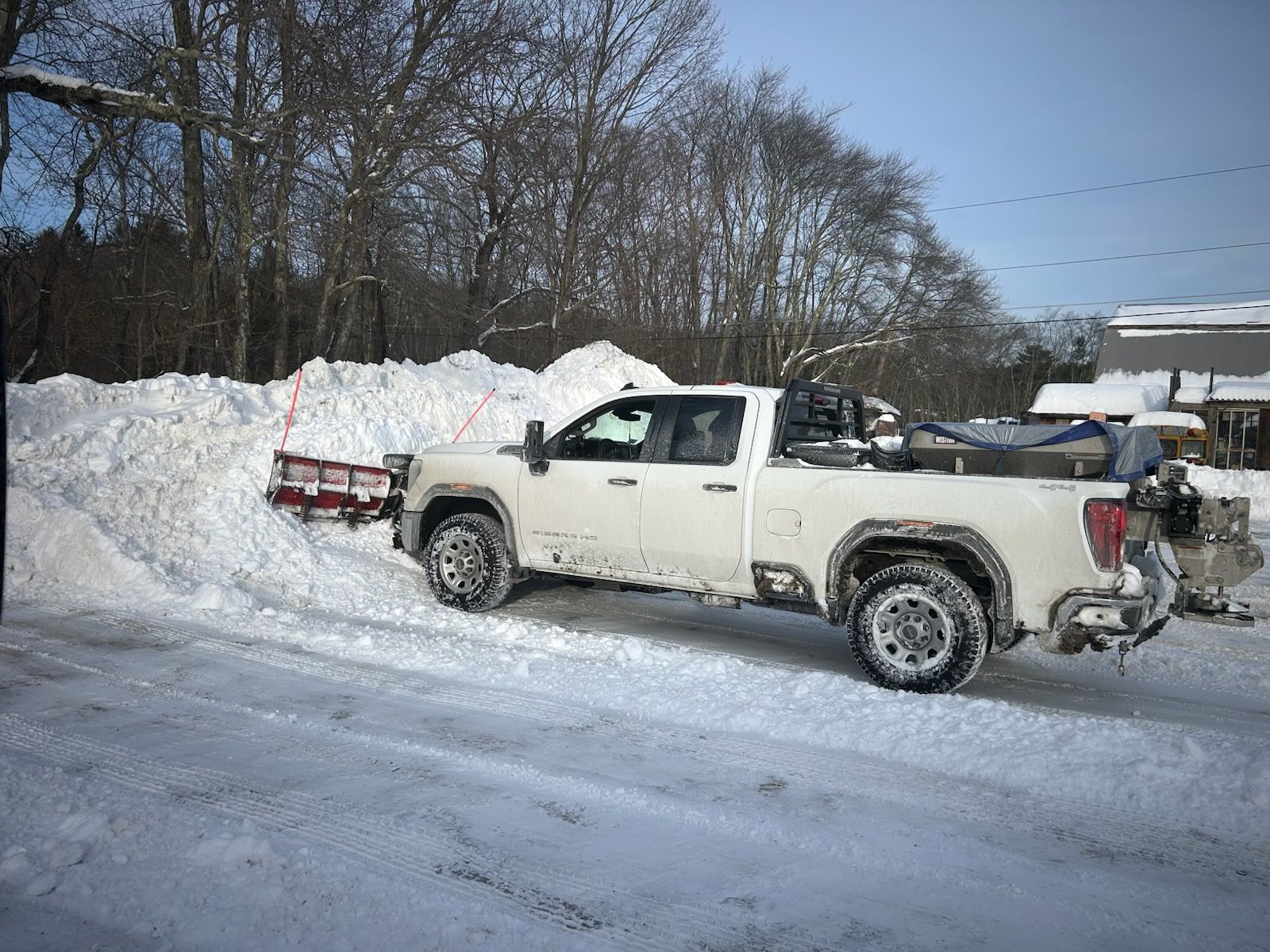 White pickup truck pulling a red plow in a snowy roadside scene