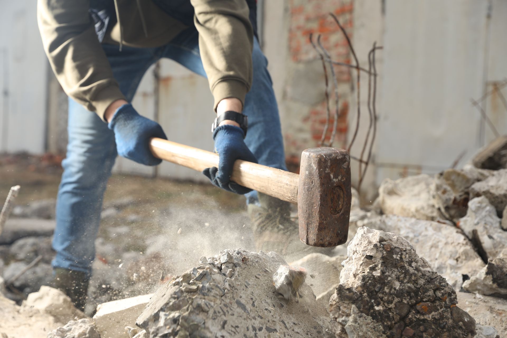 Worker using a sledgehammer to break concrete rubble on a construction site