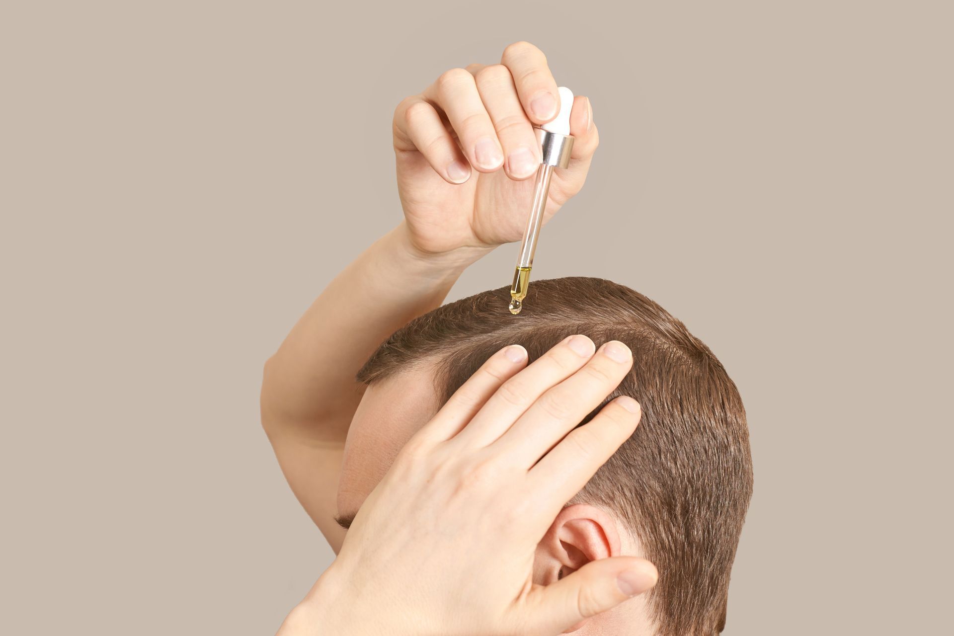 A man is applying a serum to his hair.