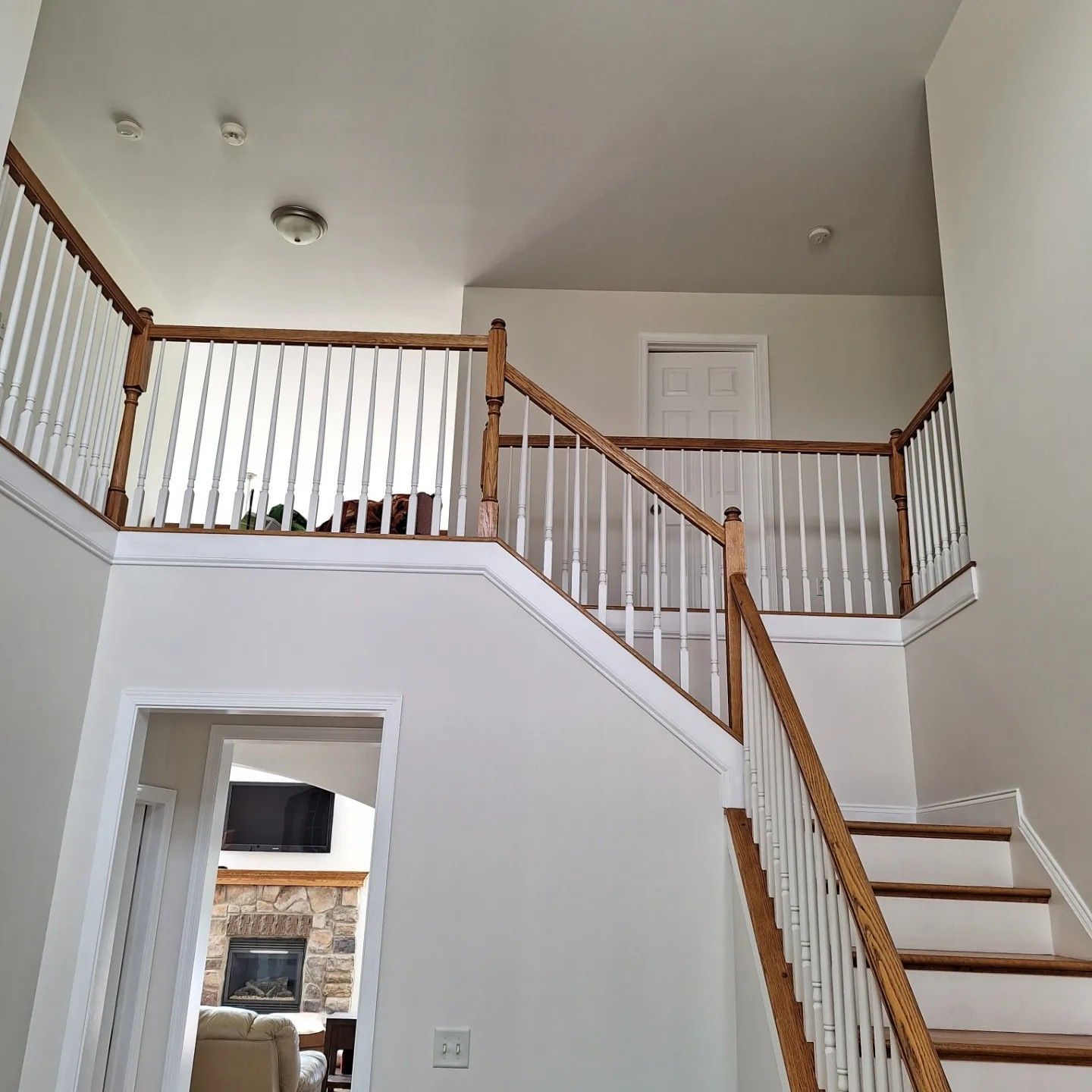 An indoor view of a two-story foyer featuring white walls, a staircase with wooden railings, and a doorway to a living room.