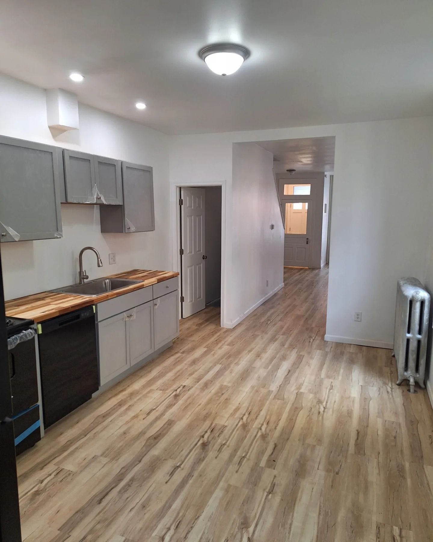A galley kitchen with light wood-look flooring, gray cabinets, a butcher block countertop, and a white radiator.