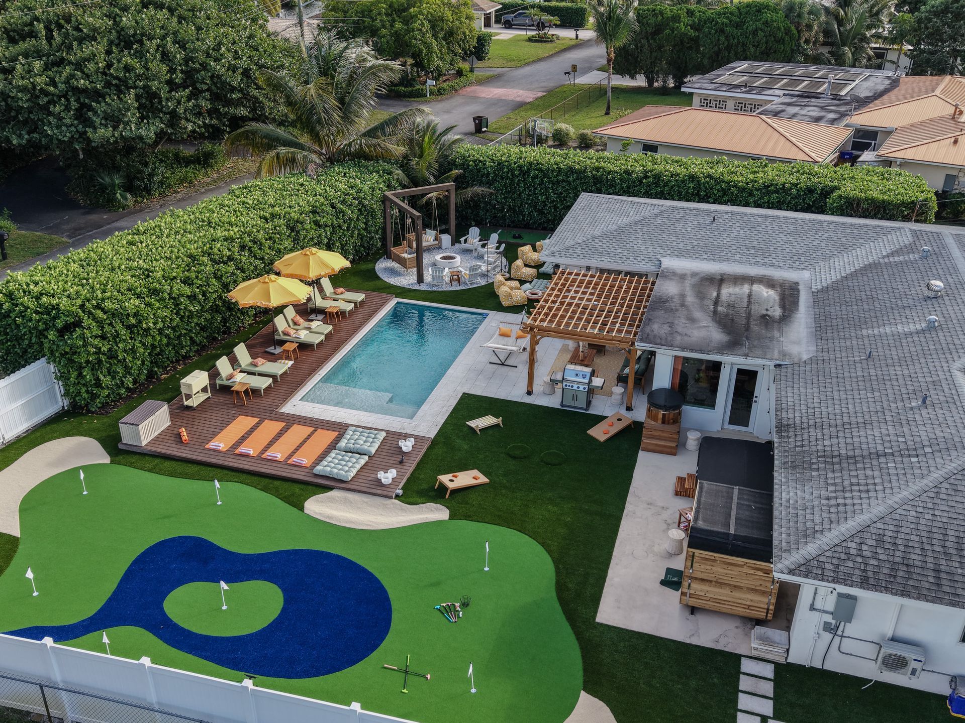 Aerial view of a backyard with a pool, putting green, patio, and lounge area.