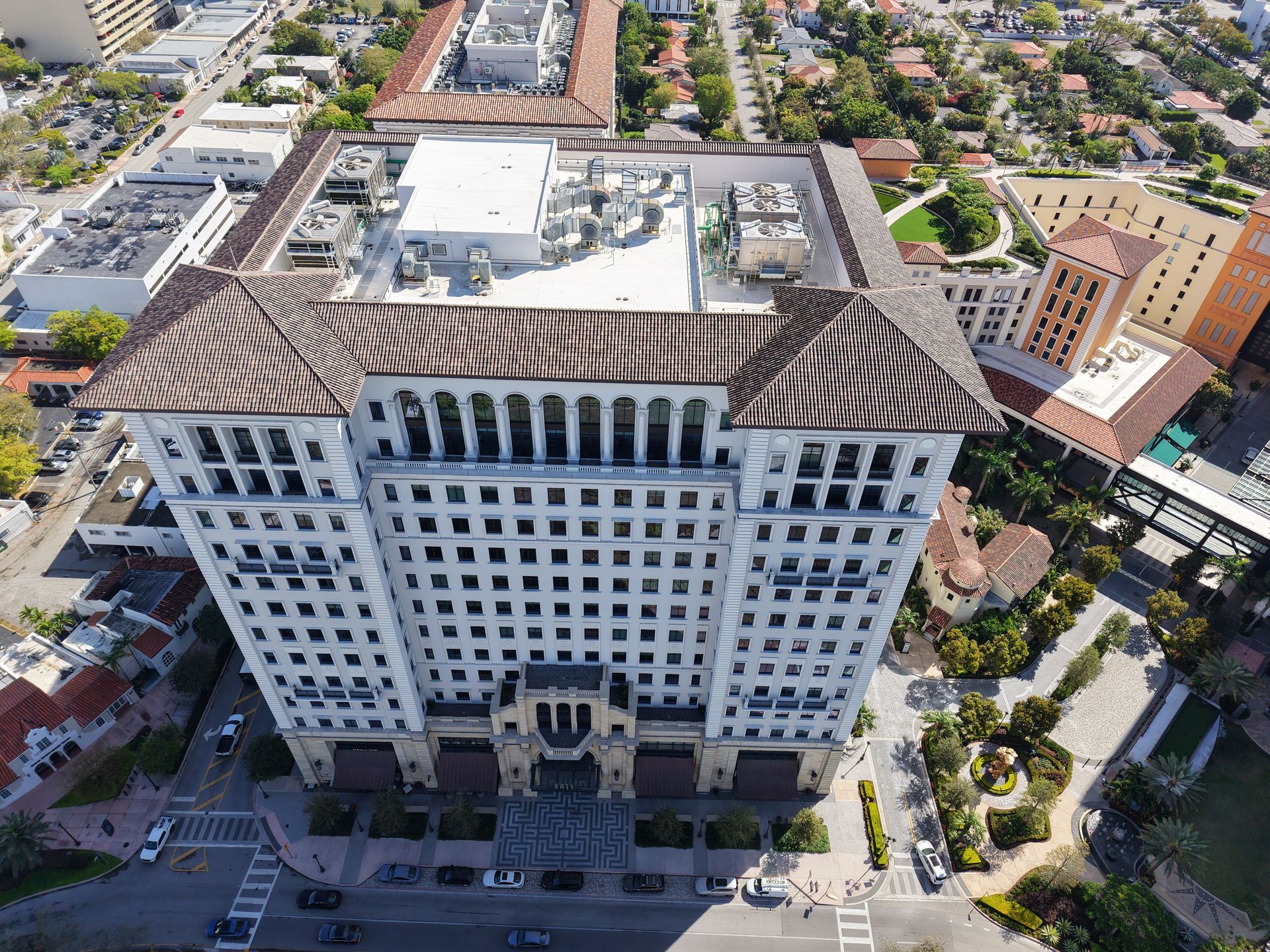 Aerial view of a white multi-story office building with a dark tiled hip roof in an urban, sunlit setting.