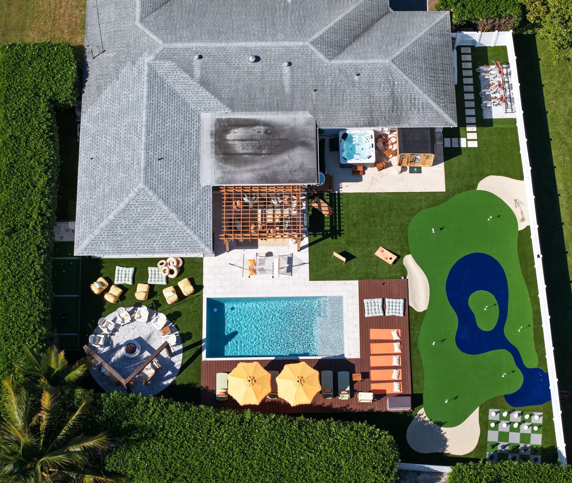 Aerial view of a residential backyard with a swimming pool, hot tub, pergola, putting green, and outdoor lounge areas.