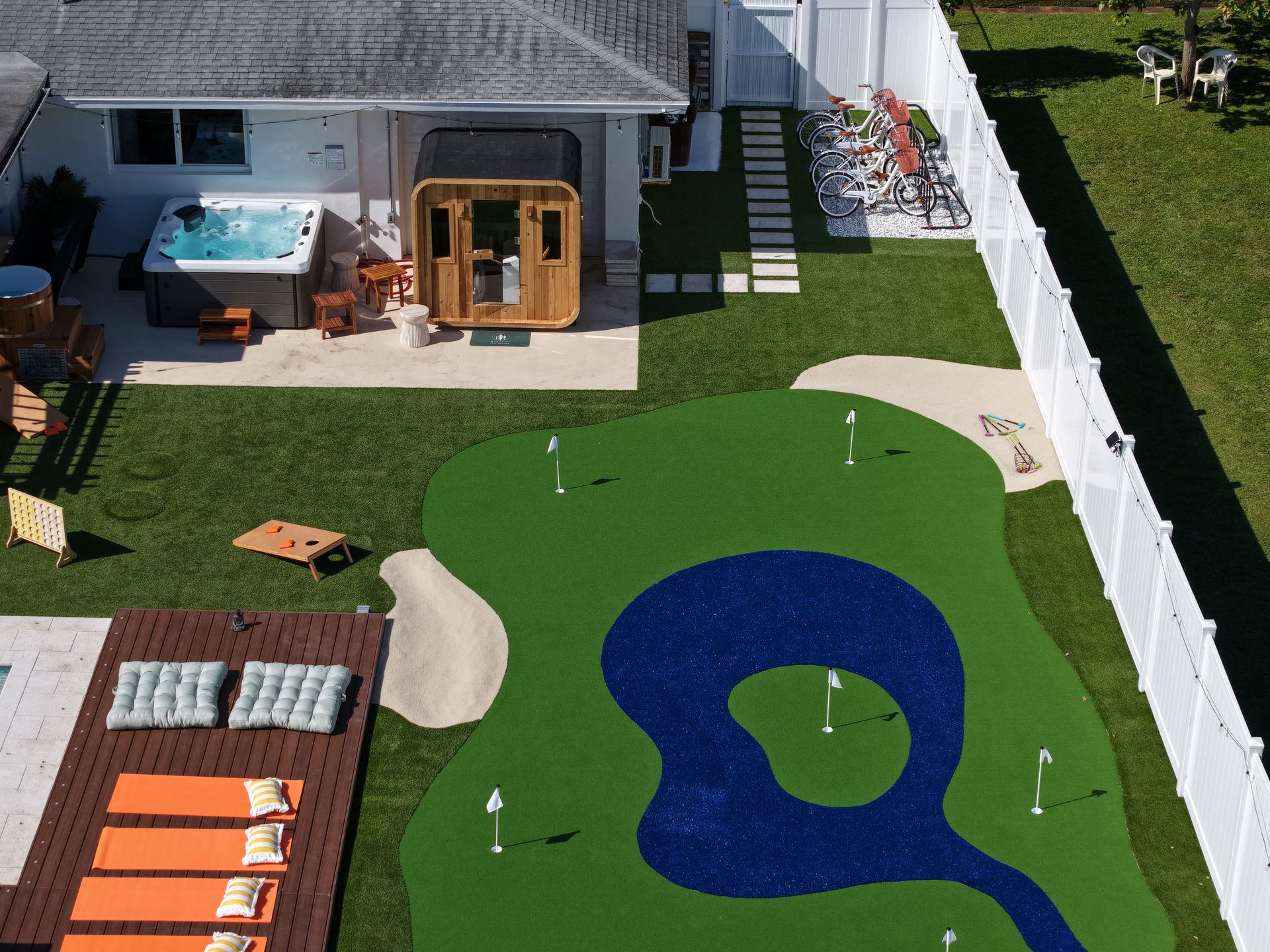 An aerial view of a backyard featuring a putting green, sand trap, hot tub, sauna, and deck with orange lounge chairs.