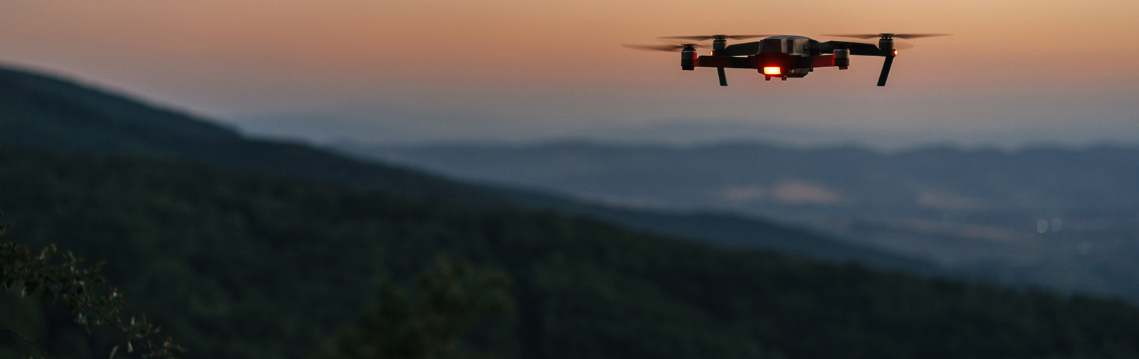 Drone flying against a colorful dusk sky above a forest.