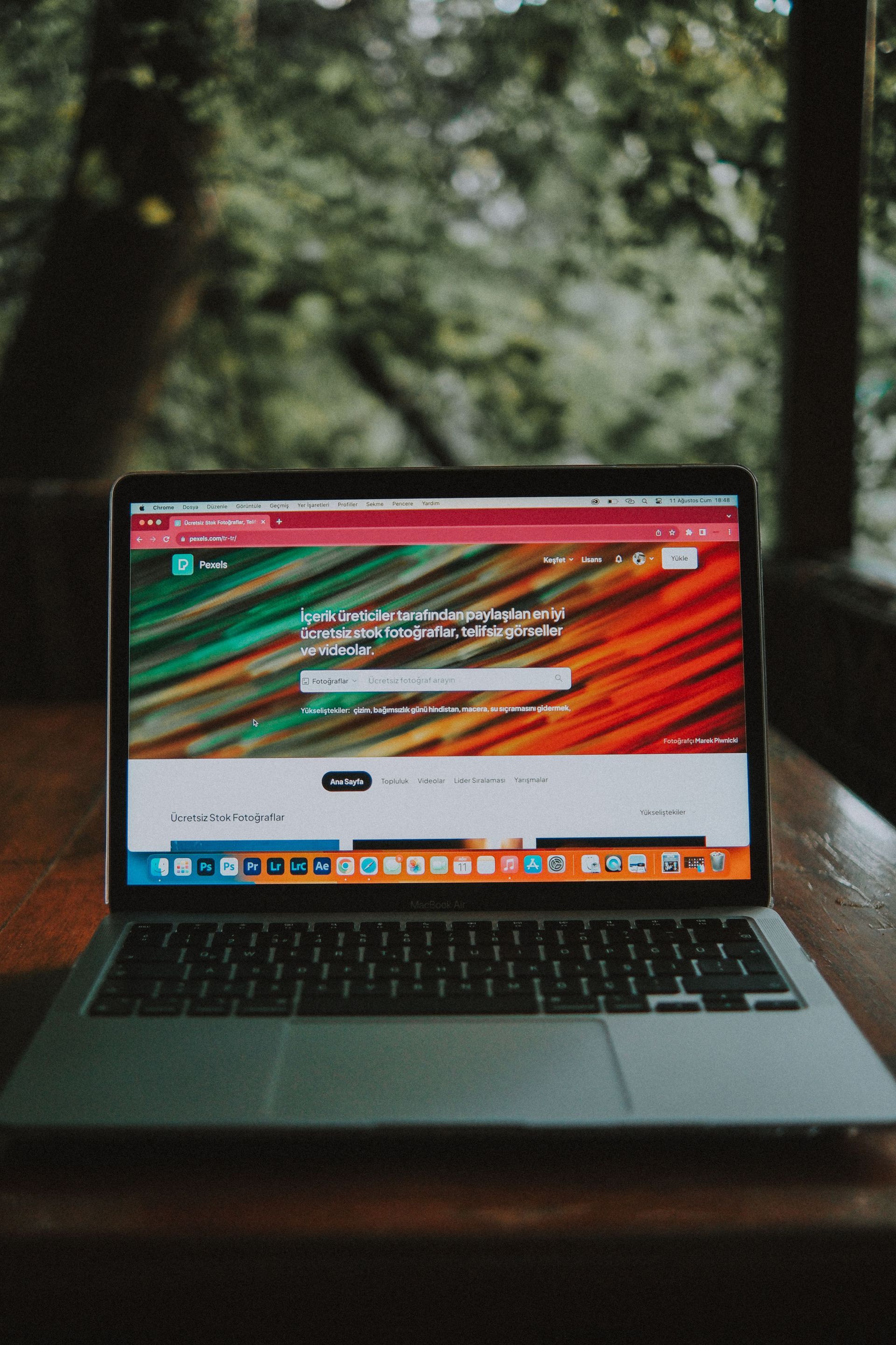 Laptop open on a wooden table outdoors, displaying a colorful webpage against a blurred forest background