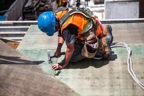 A construction worker is working on a roof with a hammer.