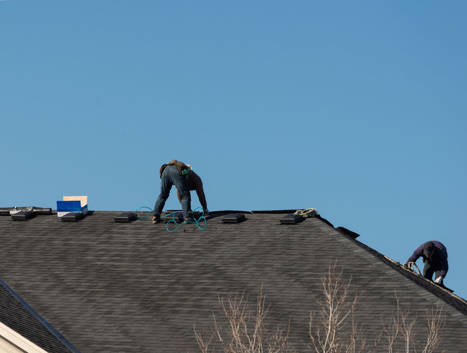 Two roofing workers on the roof replacing asphalt shingles.