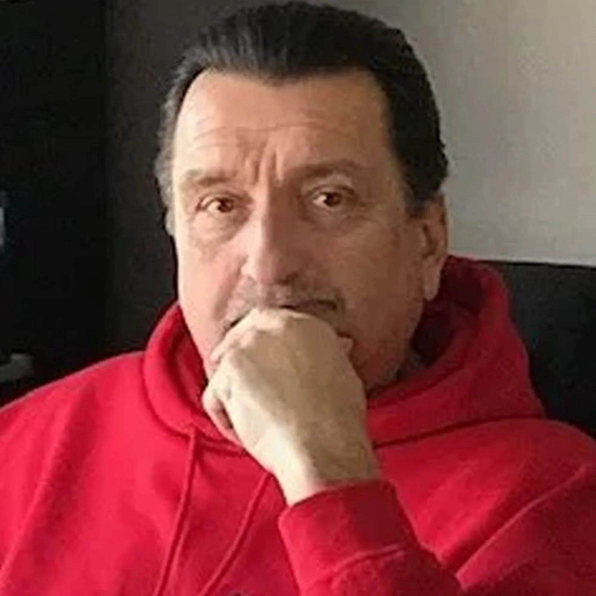 Man in a red hoodie resting his hand on his chin, looking at the camera.