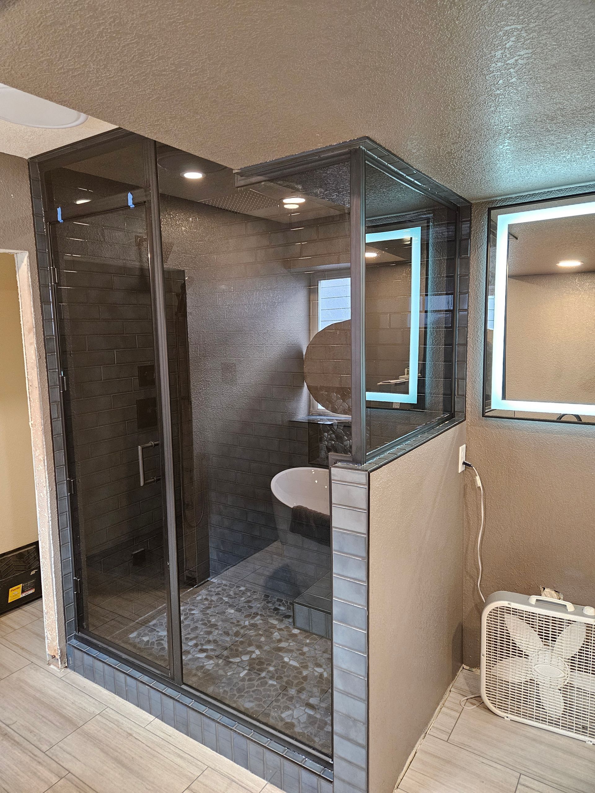Glass shower enclosure with dark tiled walls and a small window in a bathroom