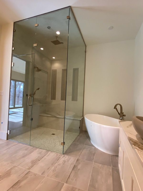 Modern bathroom with glass shower enclosure, freestanding tub, and large-format tile floor