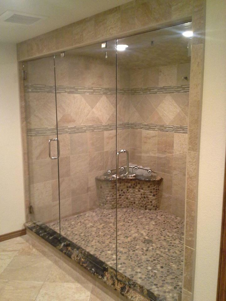 Glass-enclosed shower with beige tile and granite bench in a bathroom