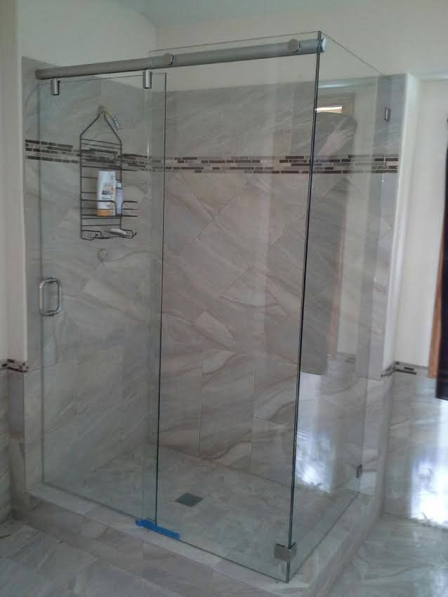 Clear glass shower enclosure in a tiled bathroom with a sliding door and metal frame