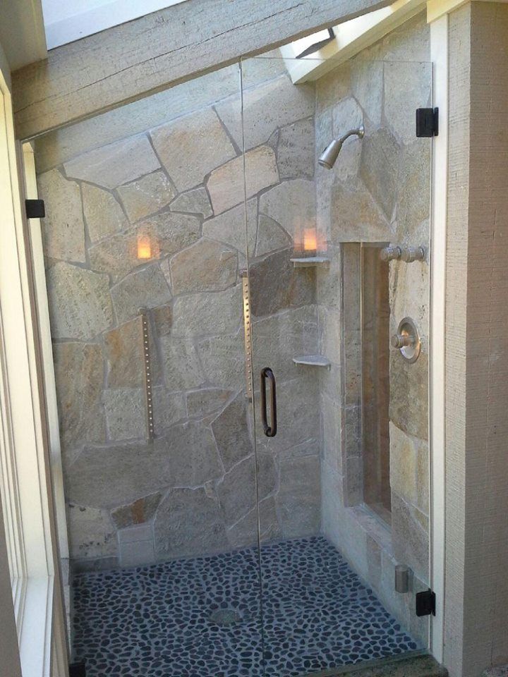 Stone-tiled glass shower enclosure with pebble floor and built-in shelves