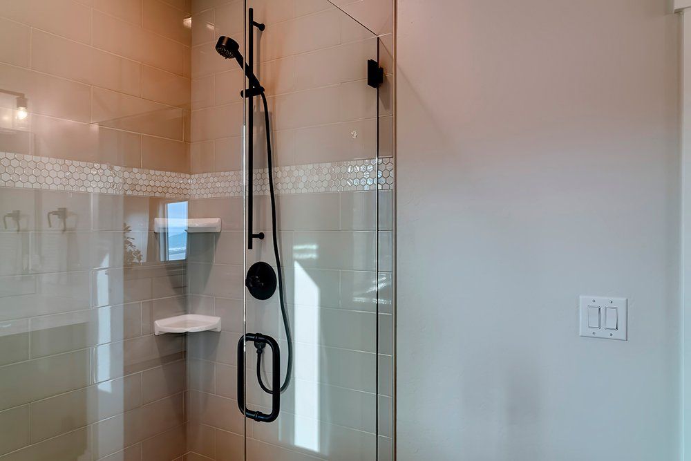 Glass shower enclosure with black showerhead and handheld wand in a tiled bathroom.