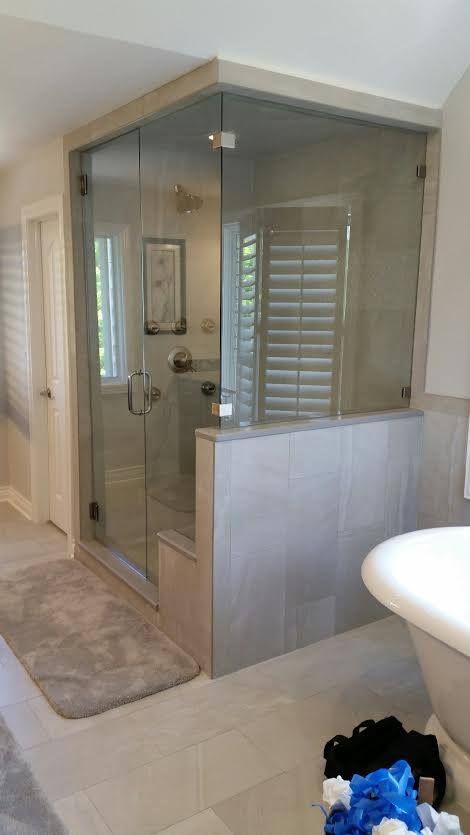 Glass-enclosed shower in a beige tiled bathroom with a sink visible at right