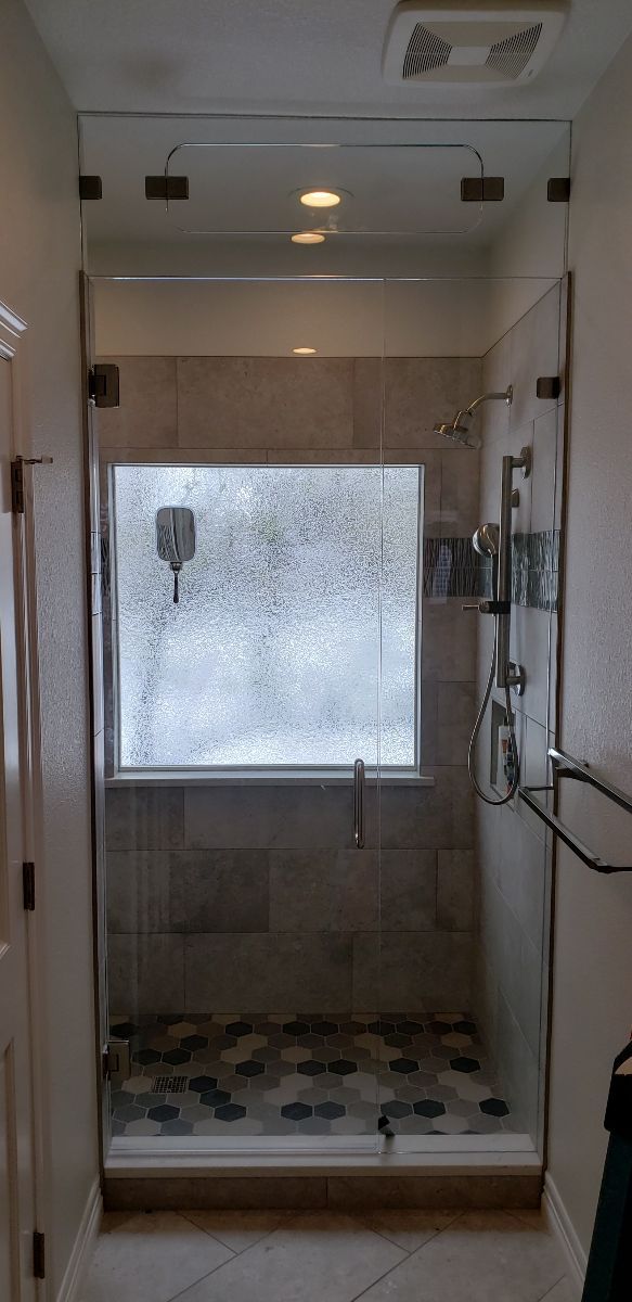 Walk-in shower with glass enclosure, wall-mounted showerhead, and pebble-pattern floor tiles