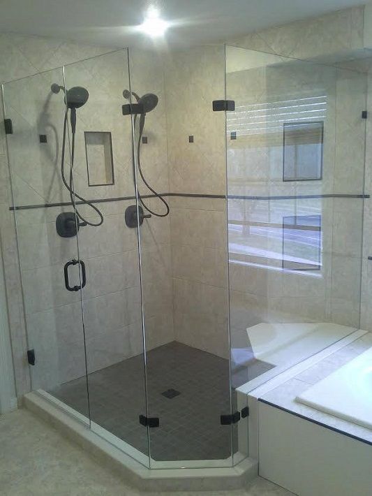 Glass shower with multiple handheld showerheads and a tiled floor in a modern bathroom