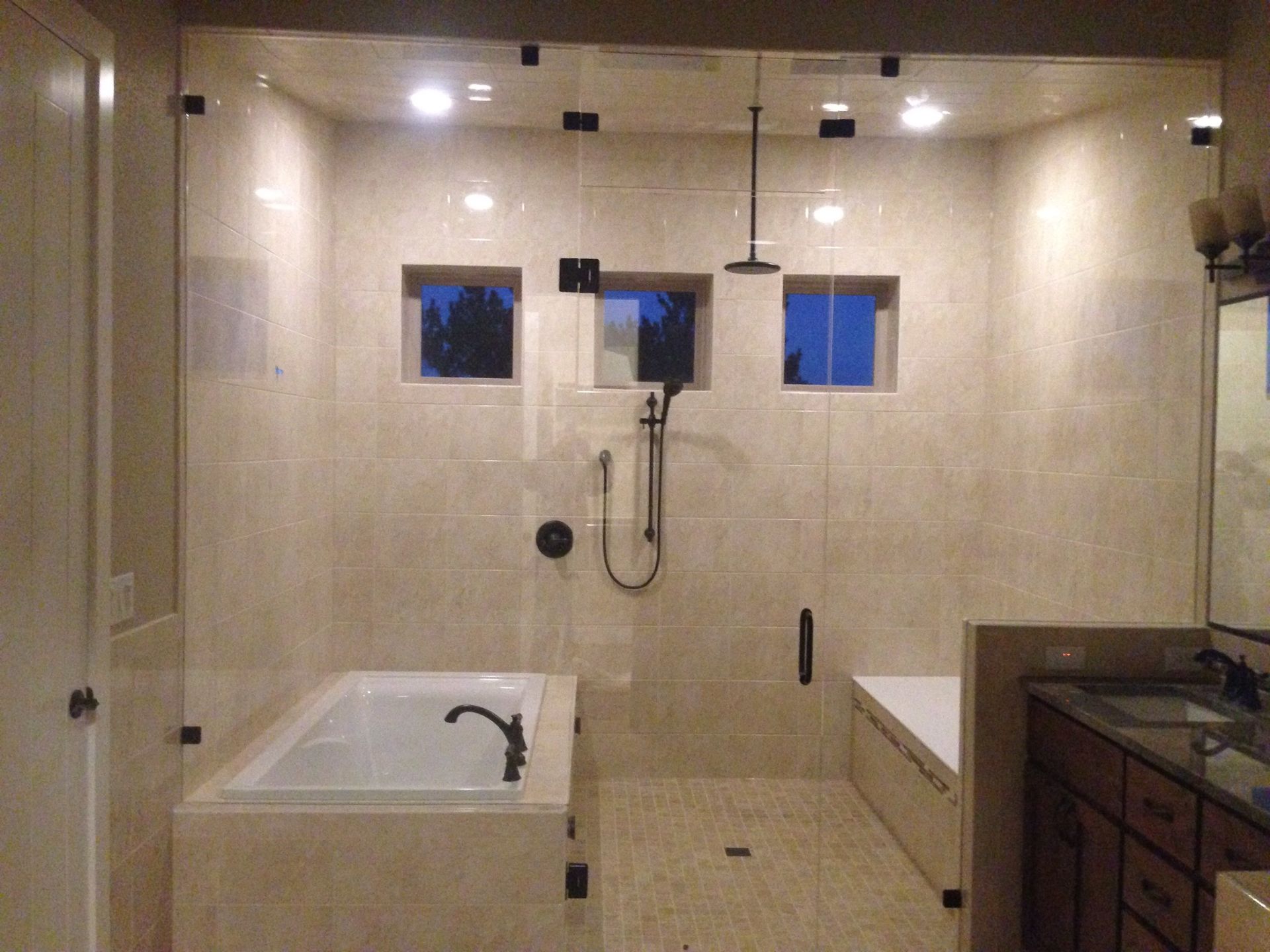 Modern bathroom with walk-in shower, freestanding tub, and dark wood vanity under recessed lights.