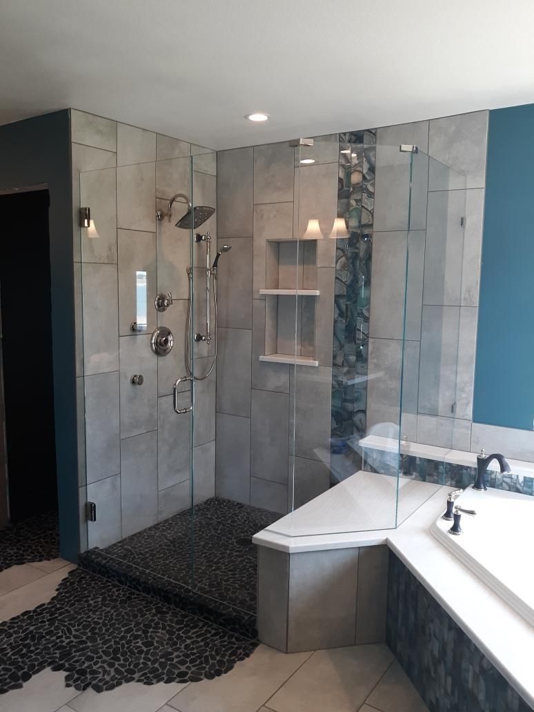 Modern bathroom with tiled shower, glass enclosure, and white bathtub beside a gray vanity.
