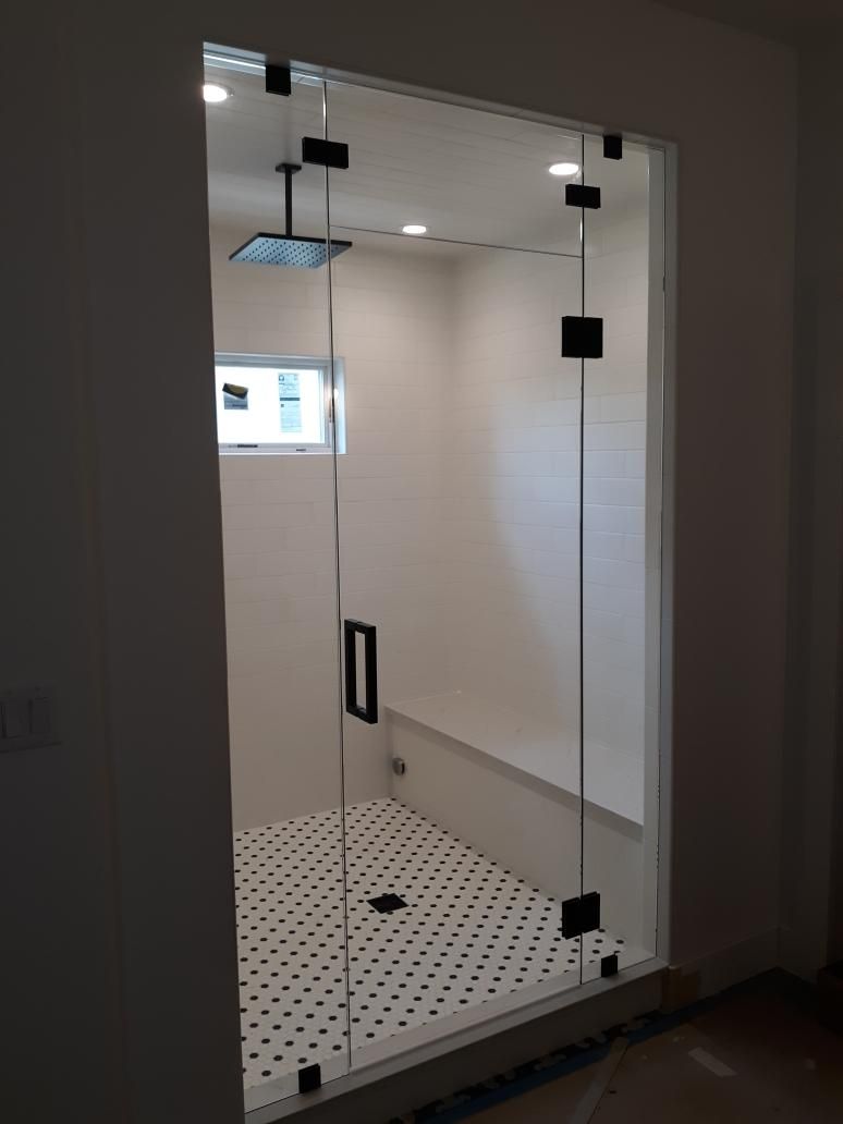 Modern glass shower enclosure with black hardware and white tile floor in a bathroom