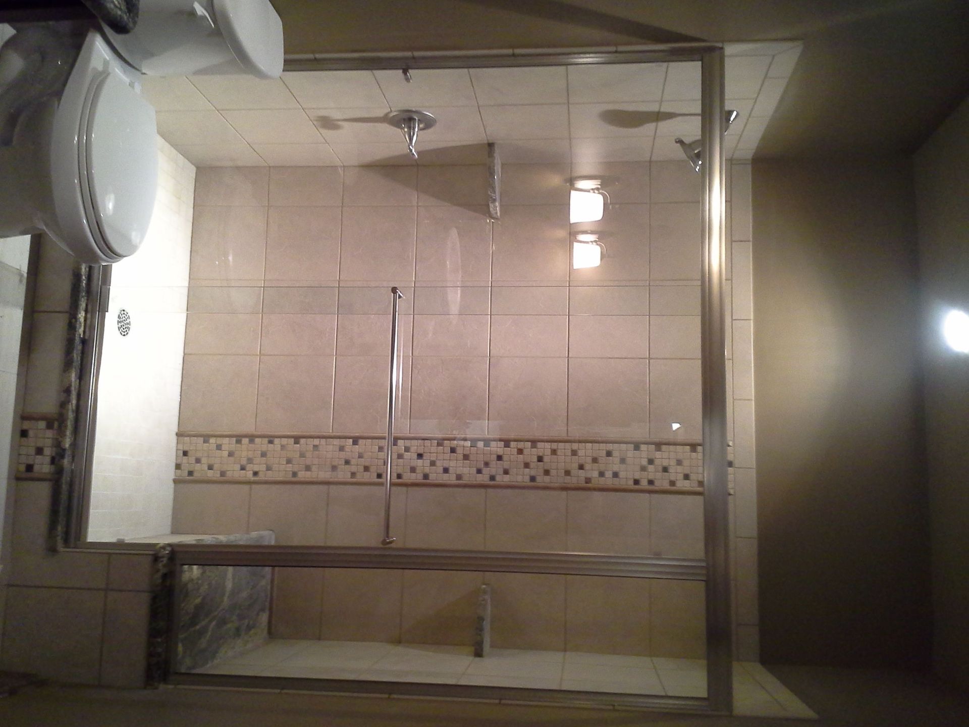 Bathroom with glass shower enclosure, beige tile walls, and a wall-mounted sink on the left.